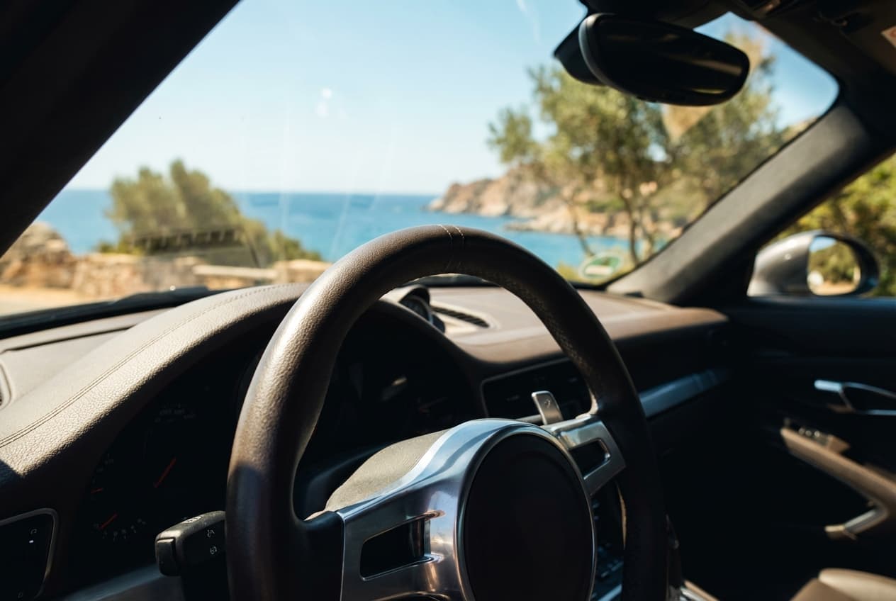Gros plan sur un volant de voiture avec un paysage sarde en arrière-plan flou